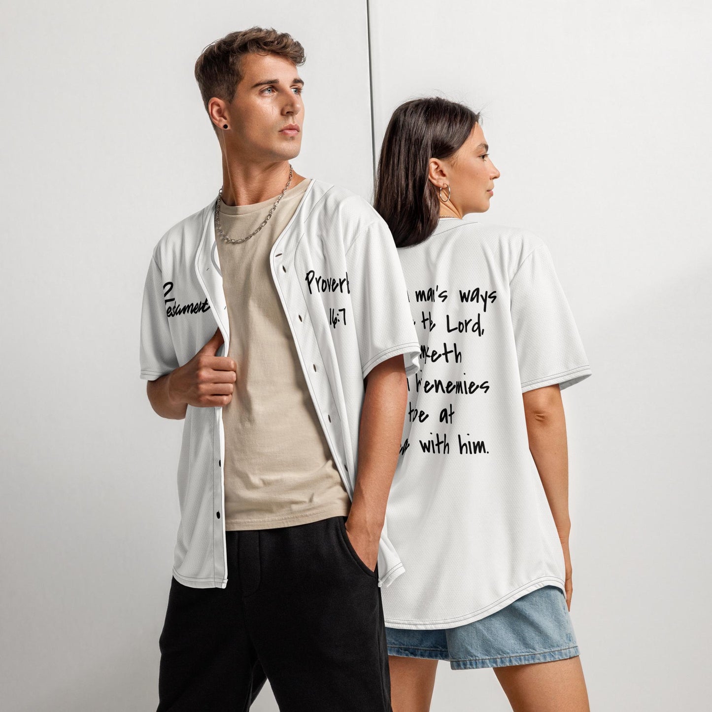 White Christian Baseball Jersey – Unisex faith-based jersey featuring “12 Testament” logo and Proverbs 16:7 Bible verse in black text, modeled by man and woman in casual streetwear style.