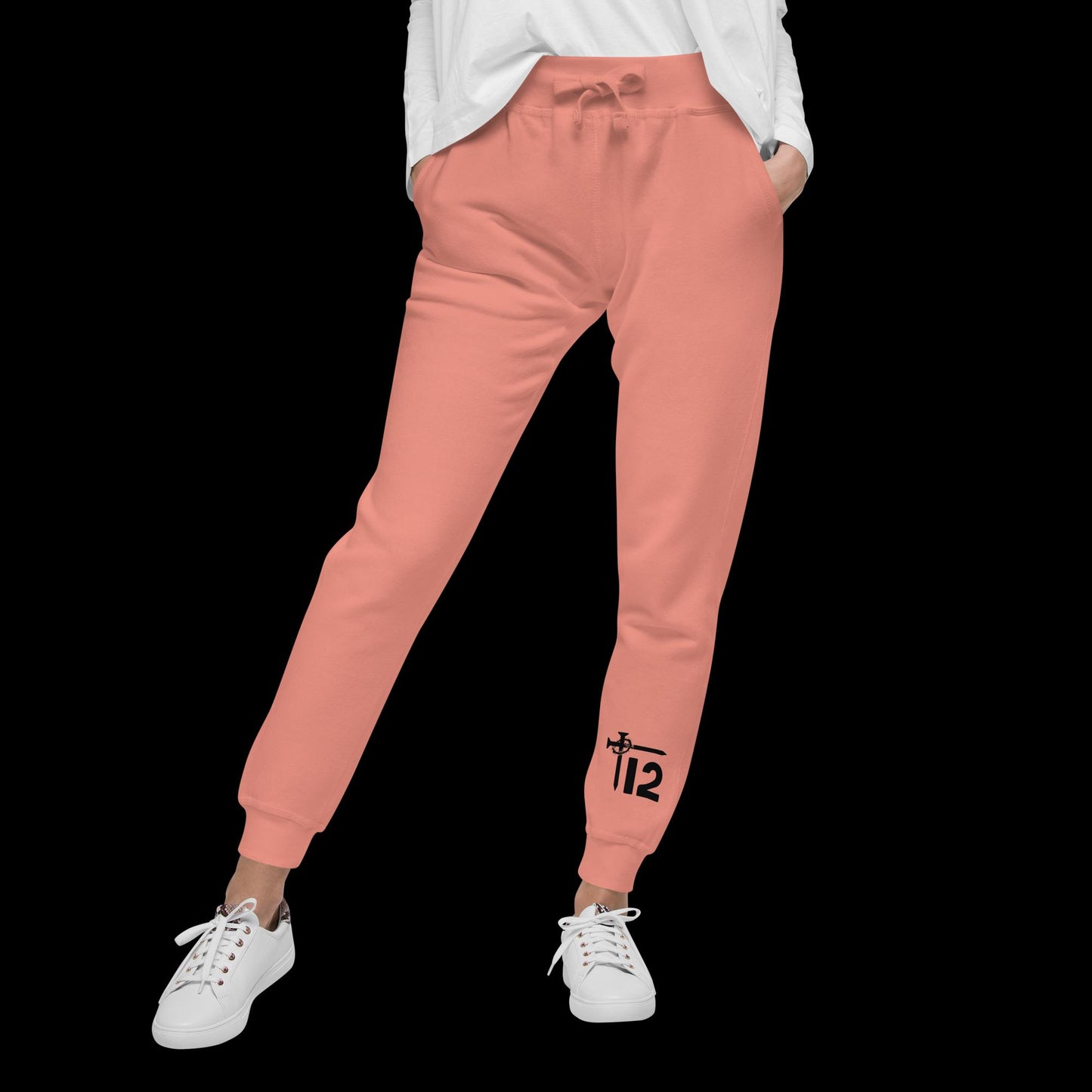 Dusty Rose Christian Sweatpants – Unisex fleece joggers featuring black “12T” logo with cross nail and crown of thorns design on leg, faith-inspired loungewear modeled by woman in white sneakers.