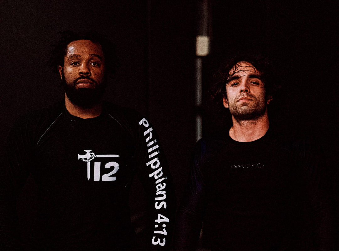 Two men wearing black long sleeve BJJ rash guards featuring the Christian verse Philippians 4:13 and T12 cross sword logo, designed for Brazilian Jiu-Jitsu grappling training and Christian faith-based athletic apparel.