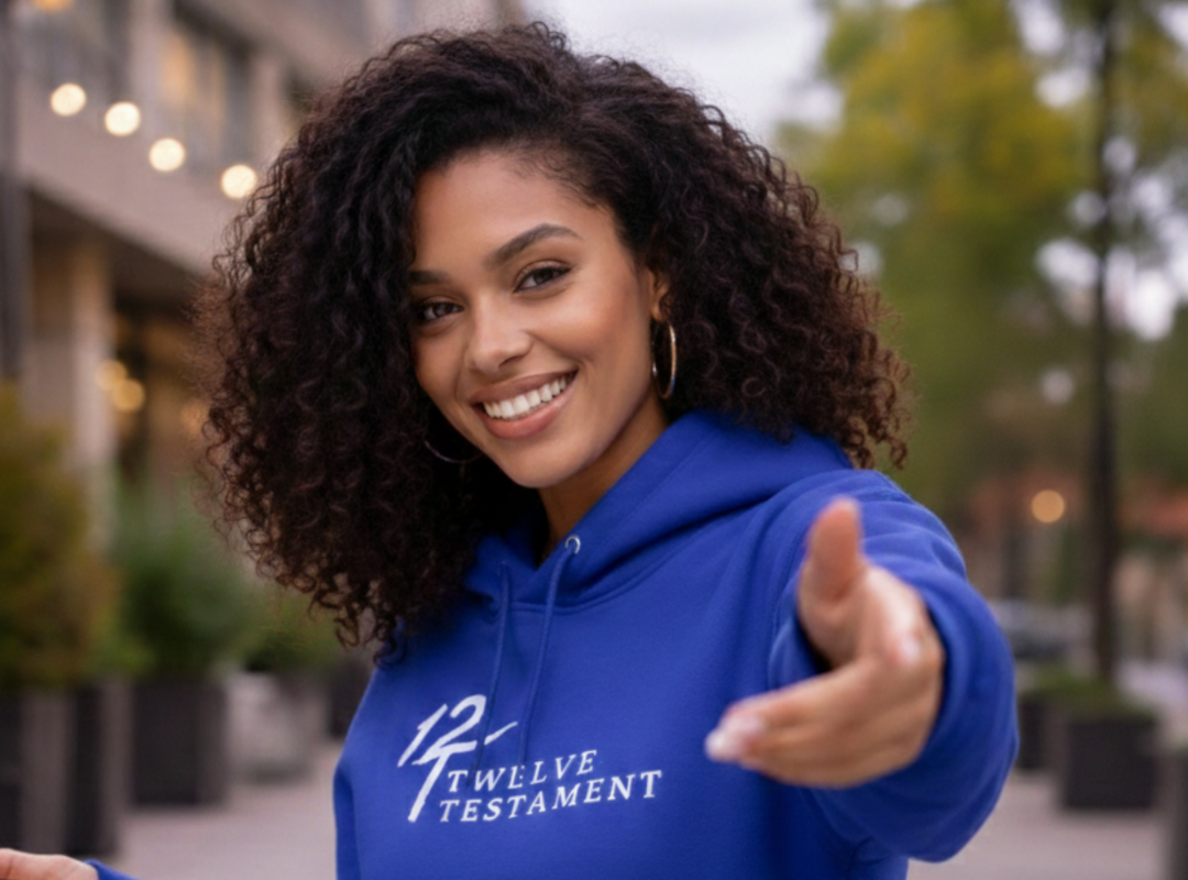 Smiling woman wearing blue Twelve Testament pullover hoodie with white logo outdoors.